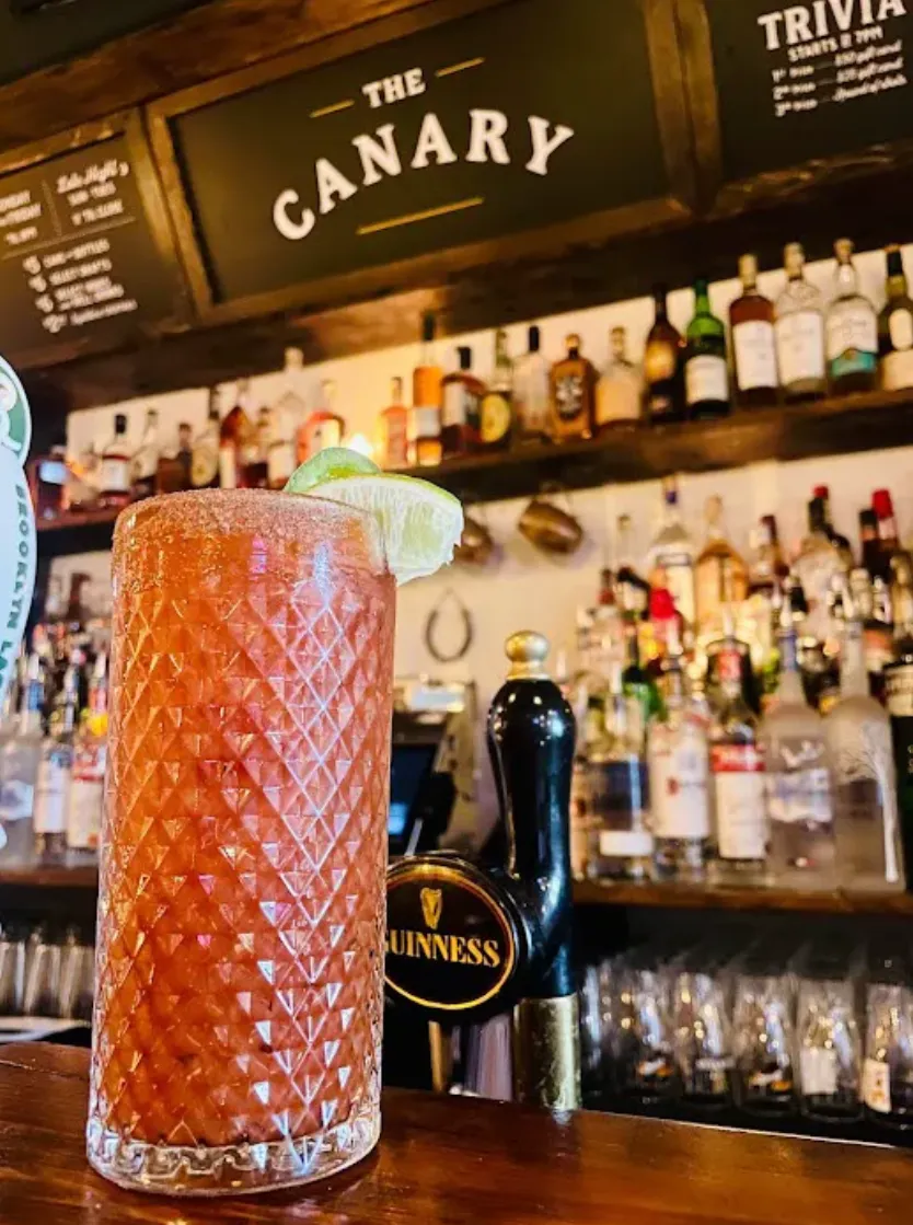A cut-glass cocktail on the bar, The Canary's painted sign behind the spirits shelf