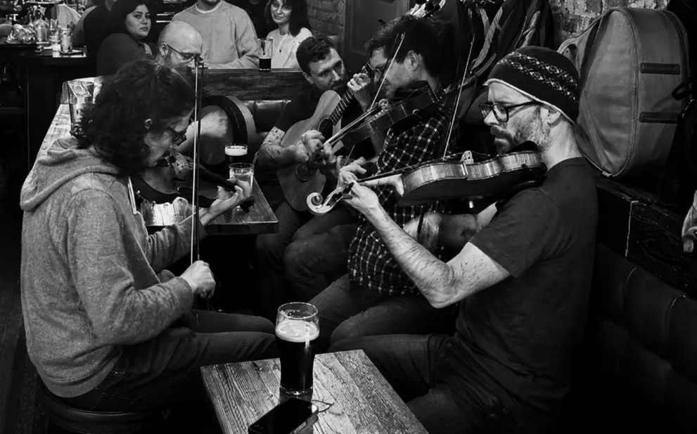 Fiddle players mid-tune at a crowded table, pints of Guinness in front